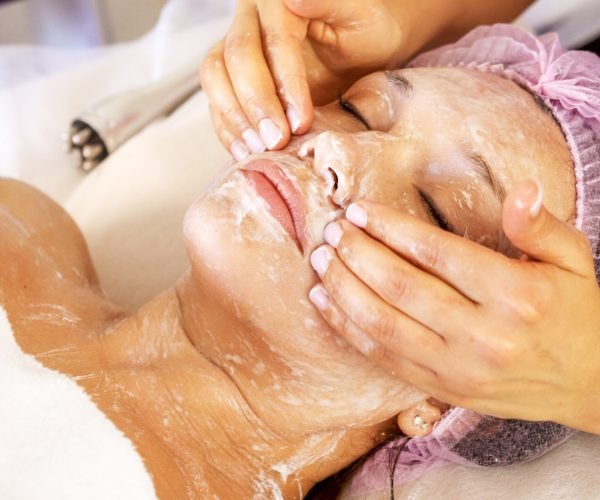 Cosmetologist applies  a moisturizing mask on female face. Woman in a spa salon on cosmetic procedures for facial care.  White woman getting beauty treatment therapy.