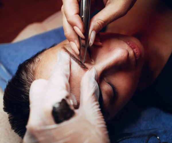 Close up of a beautician hands shaping eyebrows with tweezers to model.