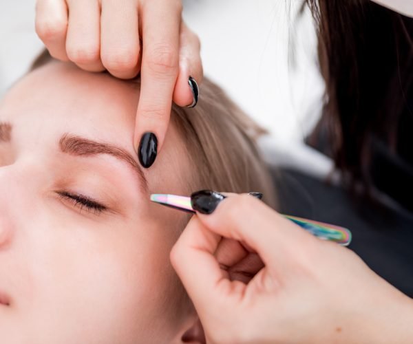 Plucking eyebrows with tweezer by beautician at beauty salon